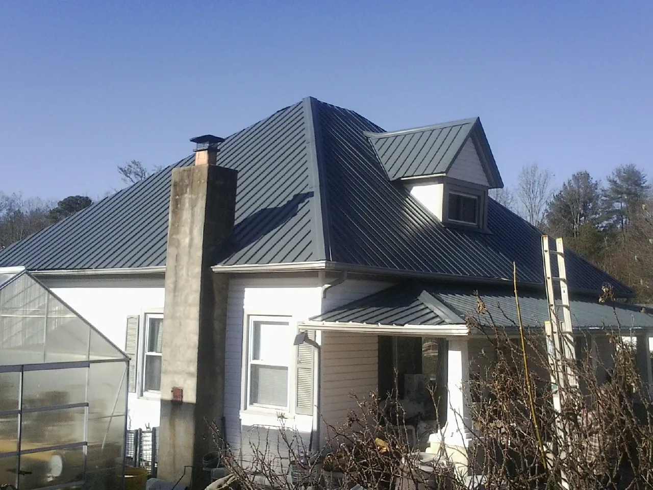 Dark blue standing seam metal roof on a white farmhouse with dormer — Slate & Tile Roof Repair by Roofing Brothers in Elmore