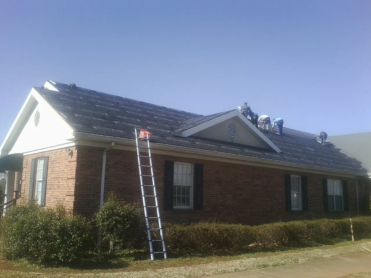 Crew tearing shingles off a brick ranch roof with a ladder set — Emergency Roof Repair work by our crew in Elmore