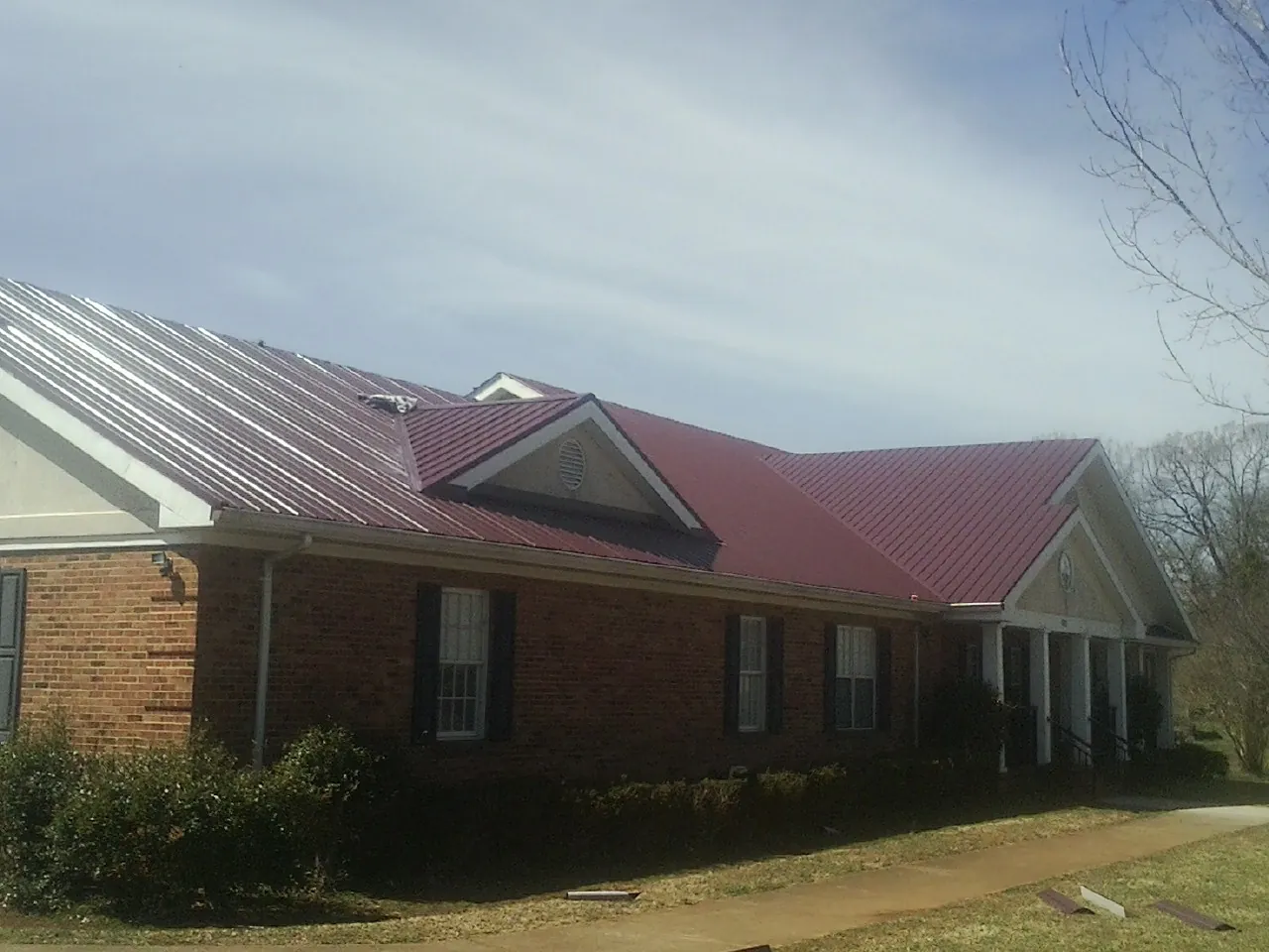 Red metal roof with gabled entries on a long brick building, from a Hail Damage Roof Repair job in Elmore