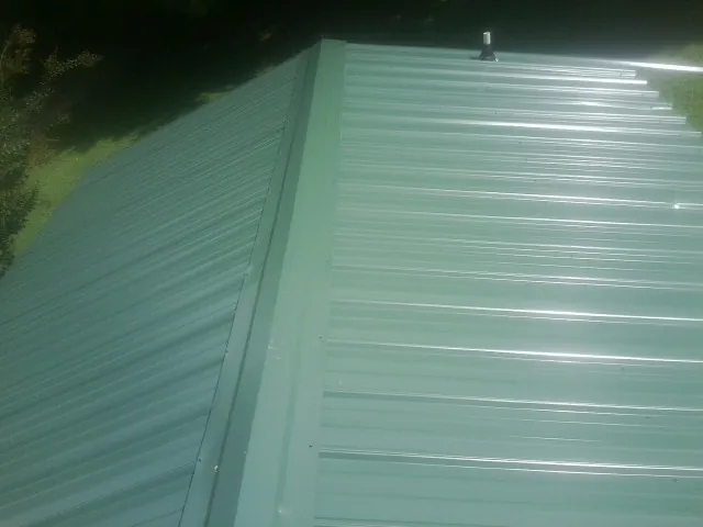 New green metal panels meeting at the ridge of a roof — Flat Roof Repair work by our crew in Elmore