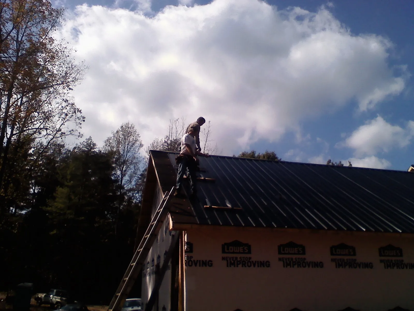 Roofer fastening dark metal panels high against a cloudy sky, from a Roof Inspection job in Elmore