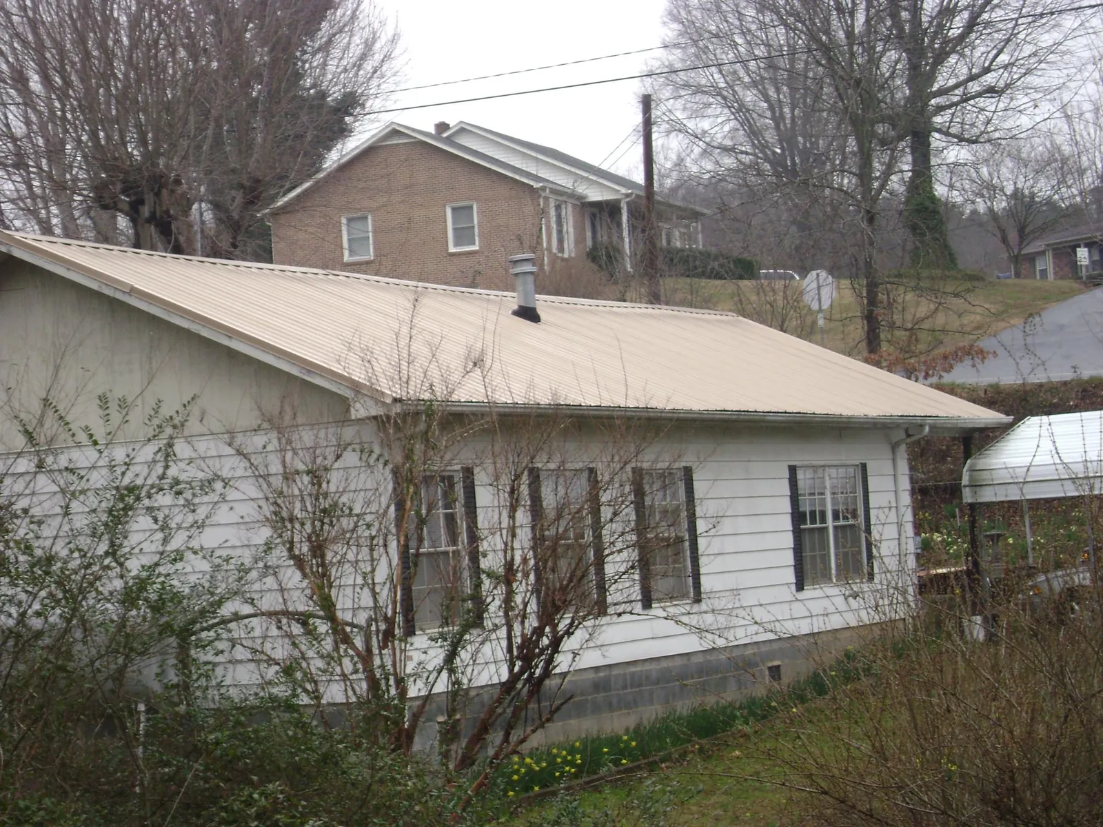 Tan metal roof on a white sided house set into a hillside — Commercial Roofing by Roofing Brothers in Elmore